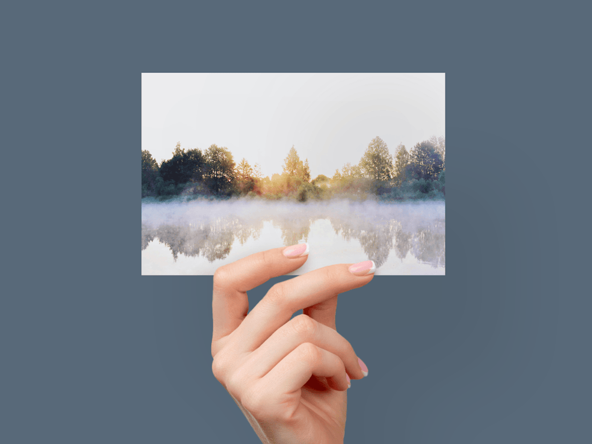 Hand holding card of forest reflected on lake