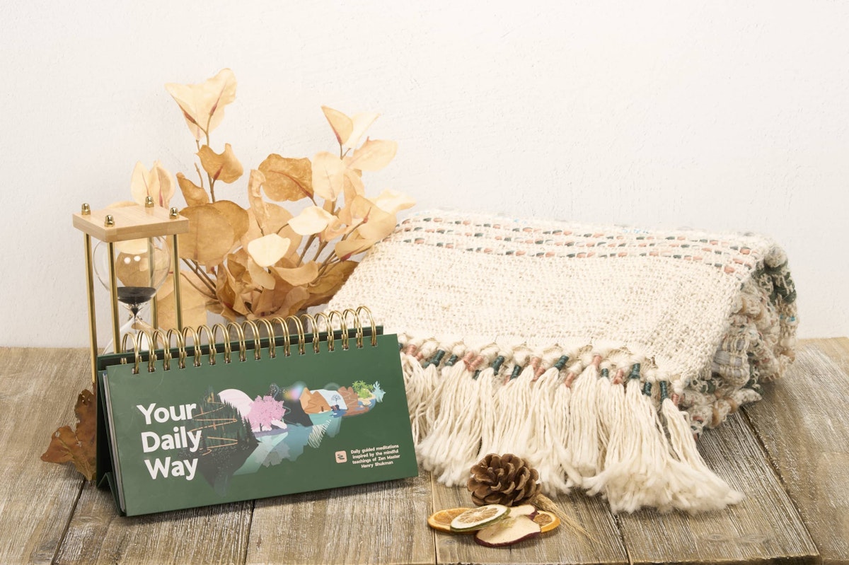"Your Daily Way" table top calendar with cream folded blanket, hourglass, and fall leaves