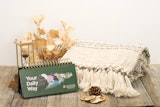 "Your Daily Way" table top calendar with cream folded blanket, hourglass, and fall leaves