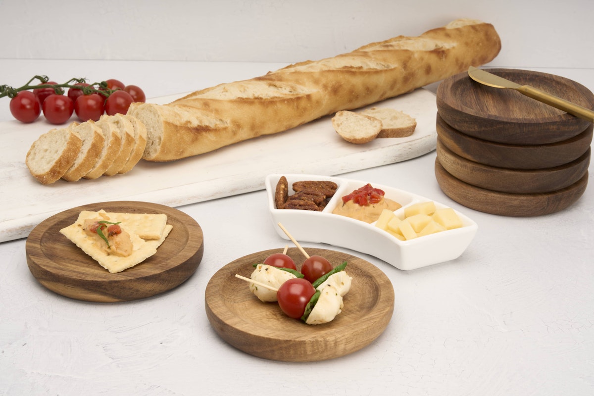 Acacia plates with baguette, cheese, tomatoes, and pecans on display