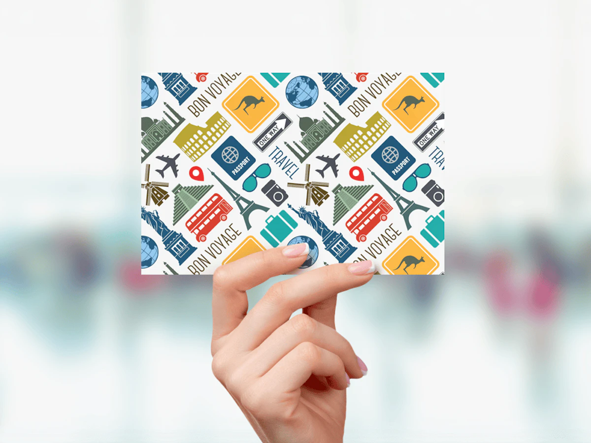 Hand holding card with international travel iconography and text 'Travel' and 'Bon Voyage'