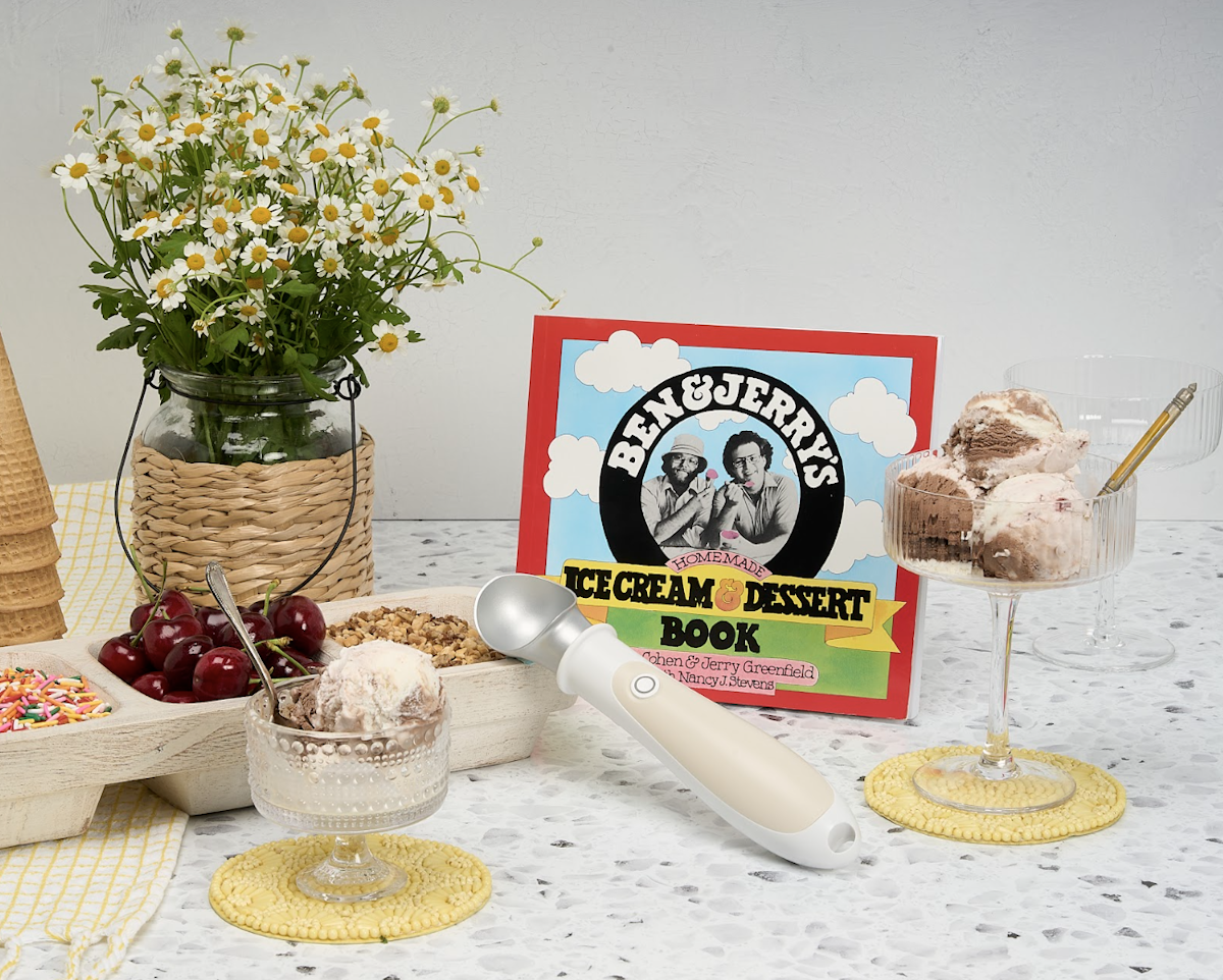 Flower vase, ice cream cones, setup for toppings including sprinkles, cherries, and nuts, with two bowls of ice cream, the heated scoop and Ben and Jerry's book