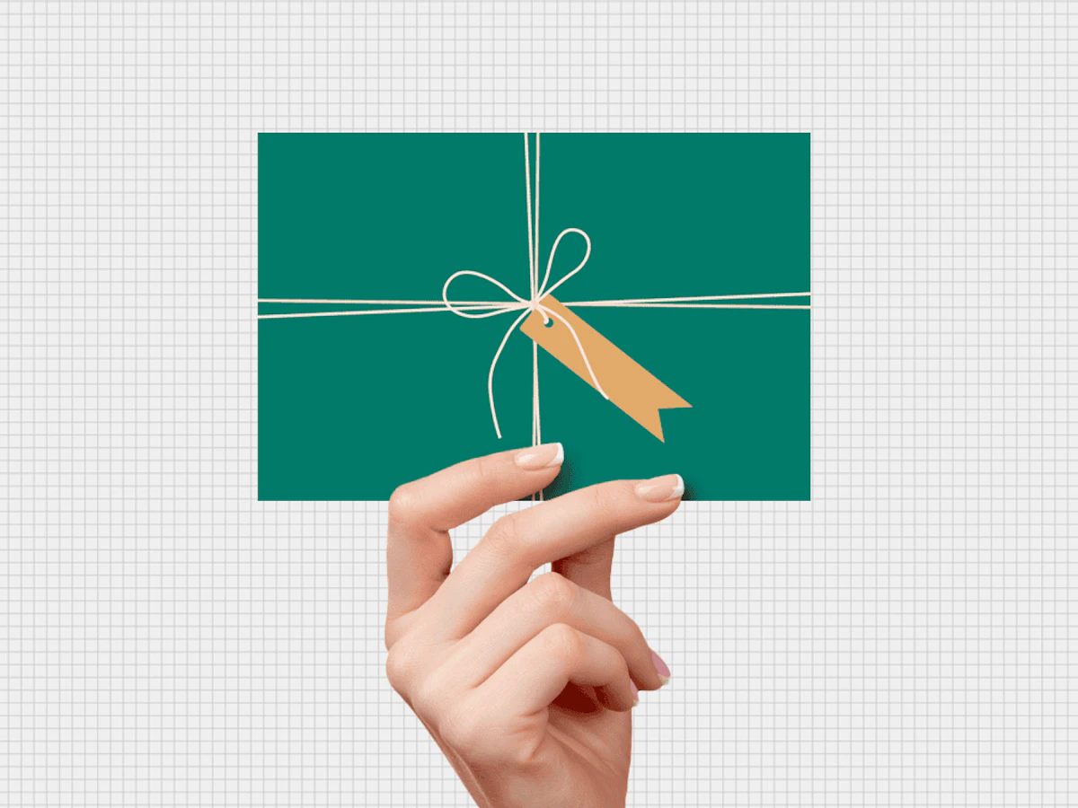 Hand holding card that looks like green present with white string bow and yellow tag