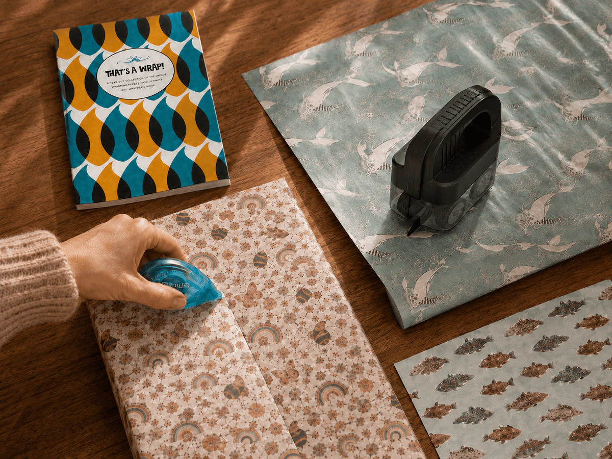 That's a Wrap book near hand taping up gift, surrounded by various gift wrap