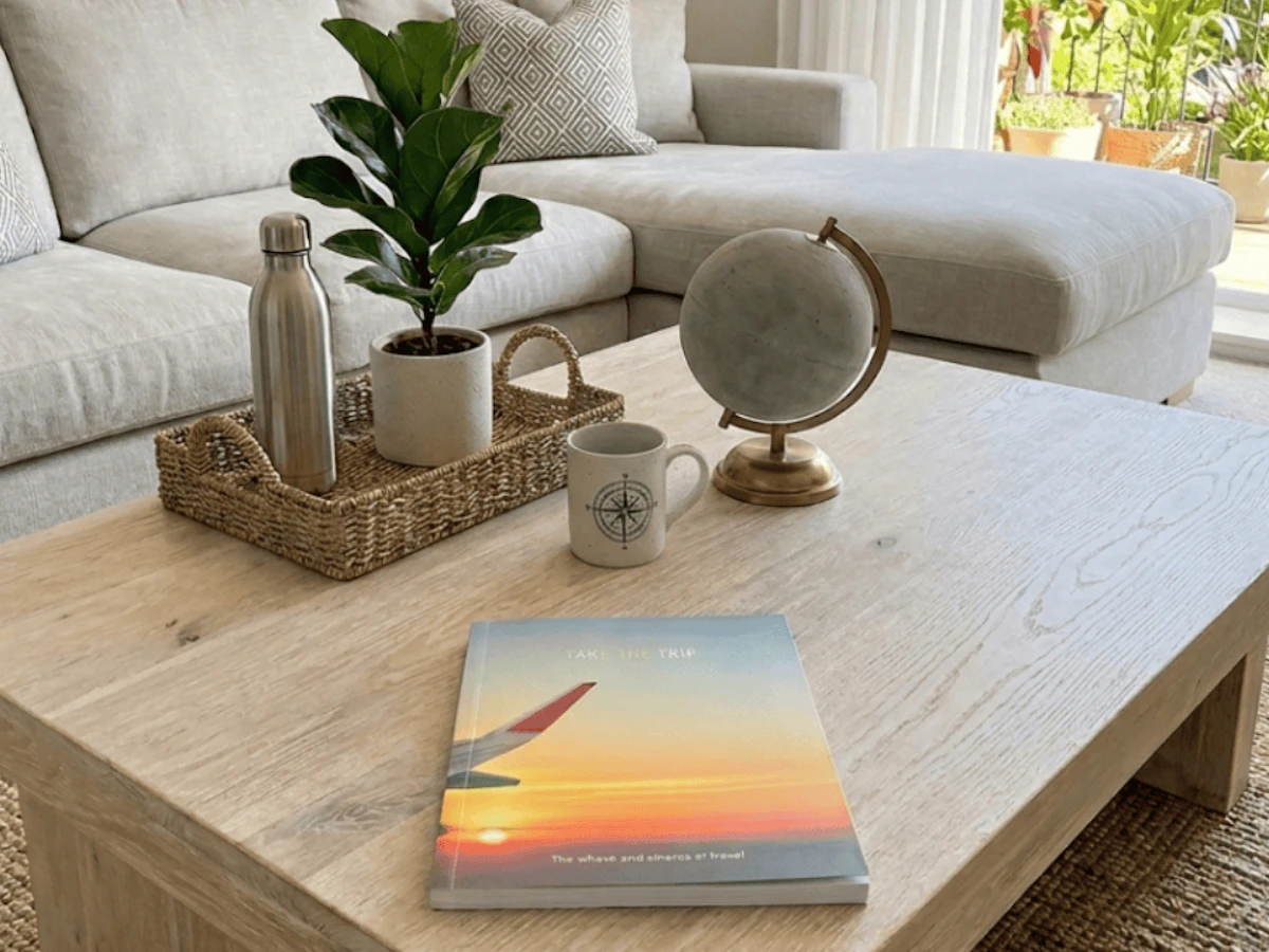 Take the Trip book on a coffee table with globe, mugs, basket, plant, water bottle