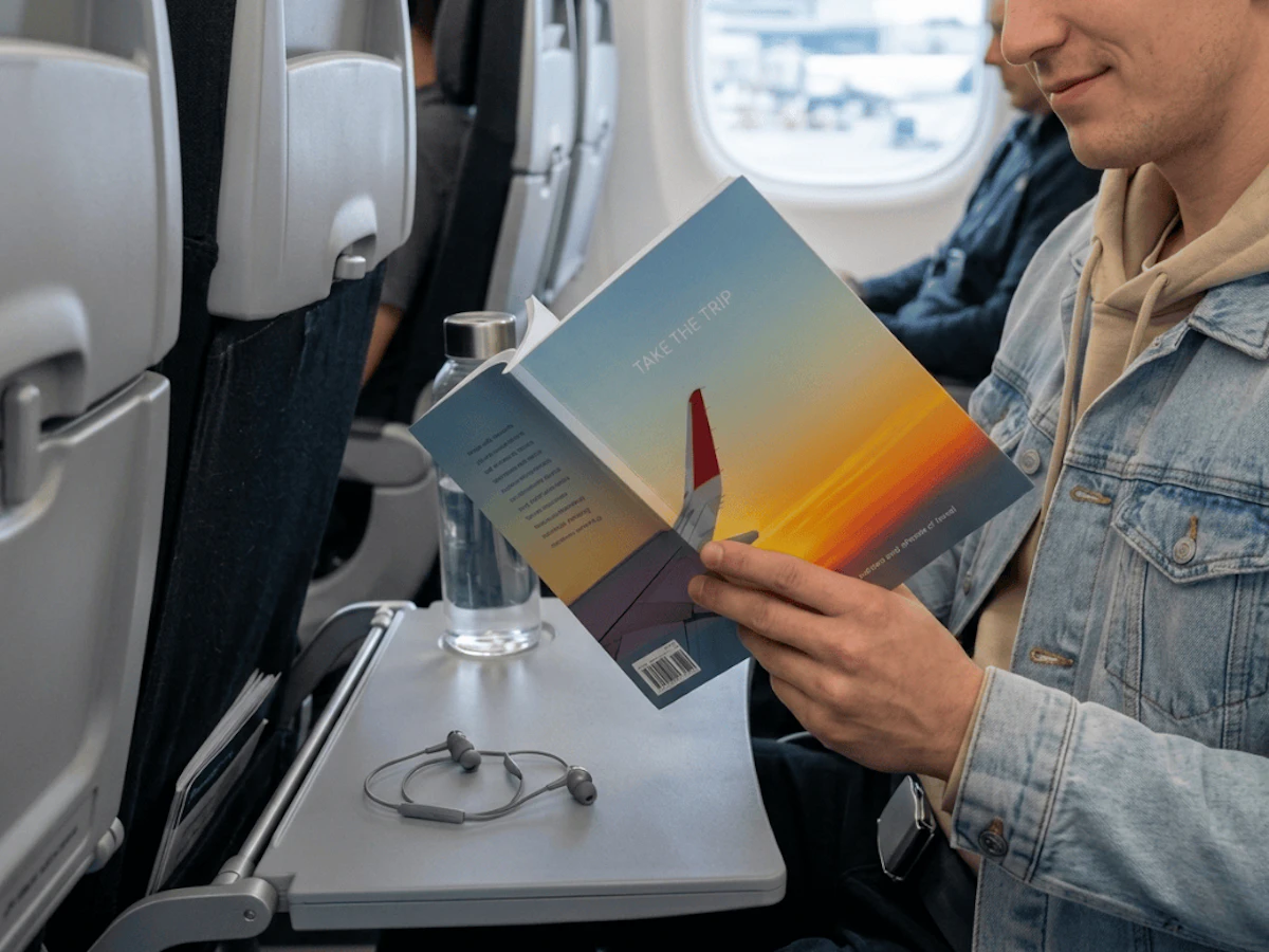 Take the Trip book being read by a person in a jean jacket on an airplane