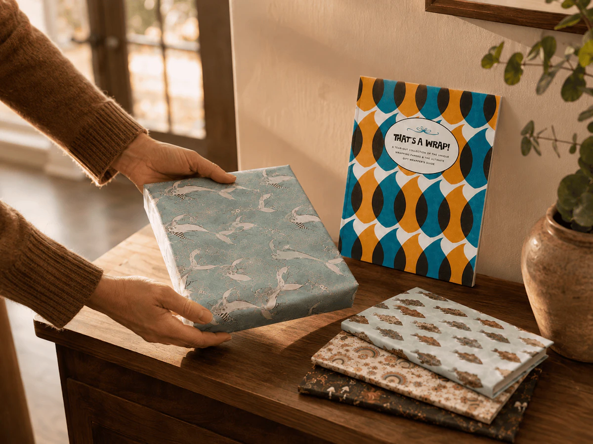 Arms setting down gift with whale wrapping paper next to other wrapped gifts and That's A Wrap book